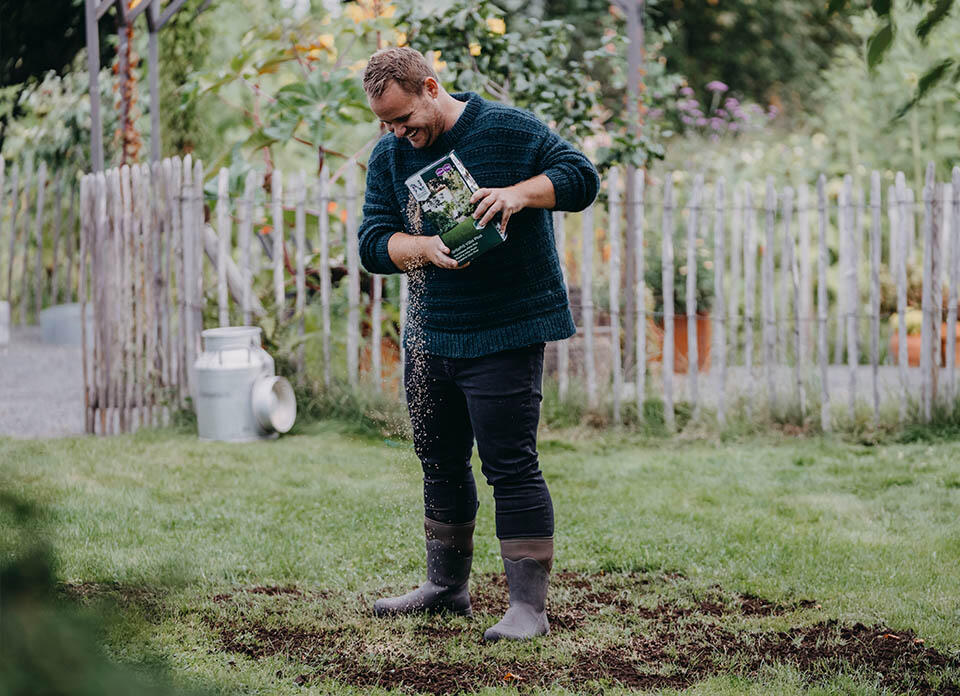 En person som står i en trädgård och sår gräs.