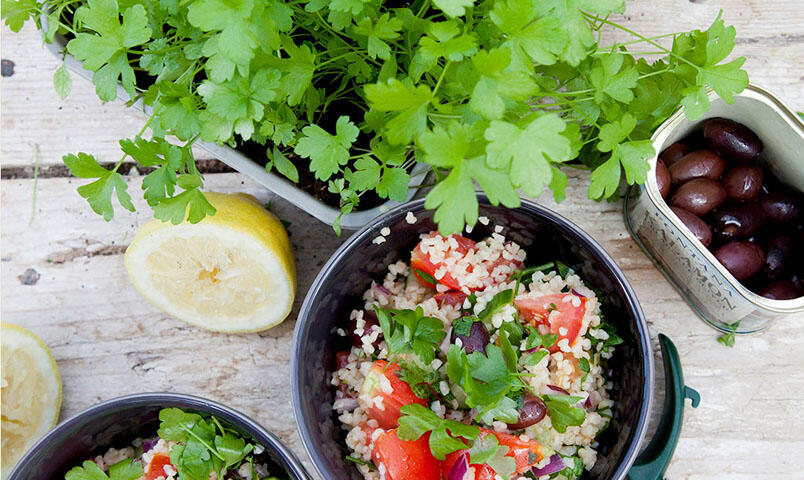 Skål med persiljesallad bredvid ett tråg med bladpersilja, citron och oliver.